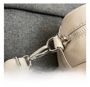 Close-up of bright silver metal hooks and zipper on a cream minimalist handbag