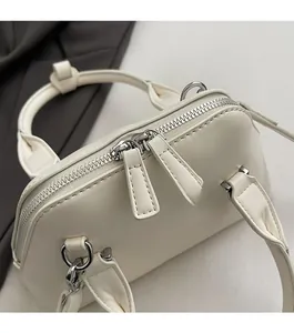 Detail of smooth silver dual-zipper closure and textured leather handle on white bag