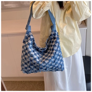 Detail of a large denim tote bag featuring blue checkered patterns and fringe textures