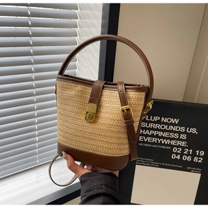 Detail der gewebten Stroh-Eimertasche mit braunem Lederbesatz und goldenem Drehverschluss