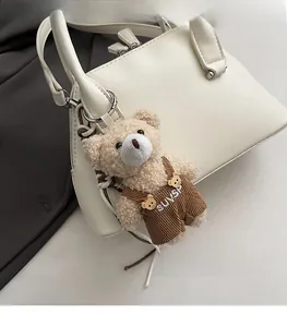 Close-up of beige plush bear charm with corduroy overalls attached to a leather bag