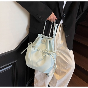 Detail of mint green bucket bag with drawstring closure and bow decoration on leather