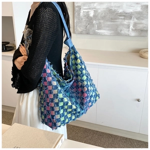 Close-up of a colorful woven checkerboard tote bag with frayed edges and knotted strap