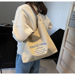 Détail du sac cabas en toile avec bandoulières en cuir marron et texte bleu artistique