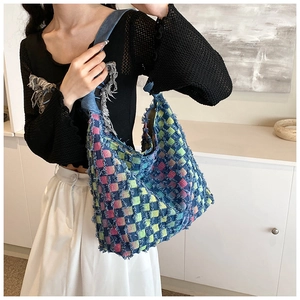 Detail of colorful woven tote bag with fringe edges shown on a model in a minimalist room
