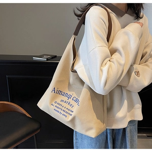 Détail du sac cabas en toile beige avec texte graphique bleu et anses en cuir marron