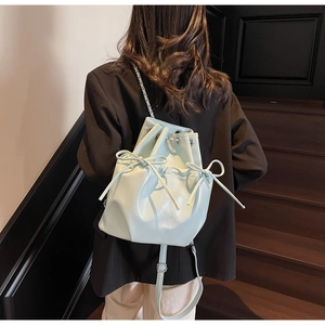Close-up of a light blue glossy bow bucket bag worn by a model in a fashion setting