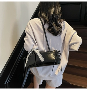 Detail of black patent leather baguette bag with white lace bow on shoulder