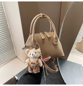 Detail of khaki Boston bag featuring a plush bear charm and adjustable shoulder strap