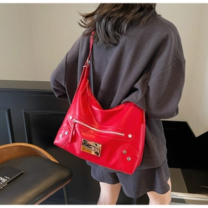 Detail view of red hobo bag with silver studs and metal plaque shown on a model's shoulder