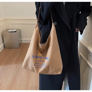 Détail d'un sac cabas en toile kaki avec typographie bleue et bandoulières en cuir marron