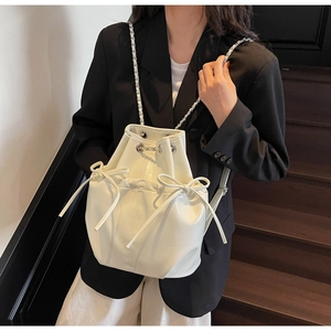 Close-up of white bucket backpack featuring bow drawstrings and metal chain straps