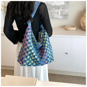 Close-up of a colorful woven checkerboard tote bag with distressed frayed edges and blue strap