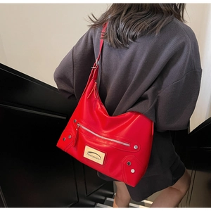 Detail of red leather tote bag showing rivet accents and silver Noronoro brand plaque