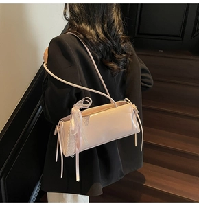 Detail of light pink patent leather baguette bag with a white lace bow on the shoulder