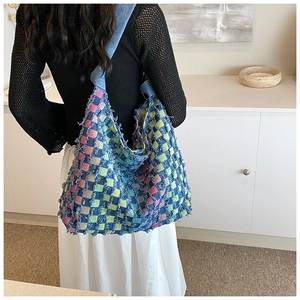 Macro shot of colorful checkered knit tote bag with distressed fringe edges and denim strap