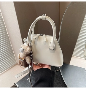 Detail of white leather bowling bag with twin handles and cute brown teddy bear charm