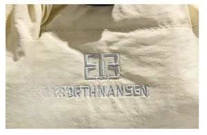 Dettaglio del ricamo del logo in argento su tessuto di nylon crema e trama fine