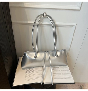 Detailed view of silver baguette bag with long handles placed on an open book