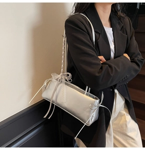 Detail of silver metallic shoulder bag with lace bow decoration worn by female model