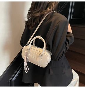 Détail d'un mini sac bowling beige avec texte embossé et breloque à pompon chic