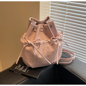 Detail of pink bucket backpack with drawstring, bows and silver chain on a leather sofa