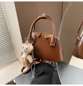 Detail of a brown leather bowling bag with a cute teddy bear charm and twin handles