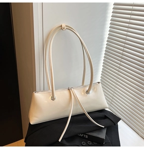Detailed close-up of cream leather baguette bag with long tassels on a black suit blazer