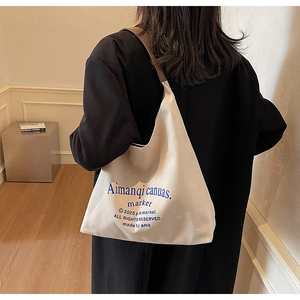Détail du sac hobo en toile blanc cassé avec bandoulière en cuir marron et texte bleu