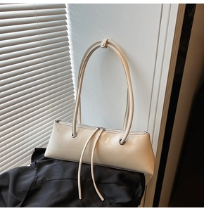 Detail of cream glossy patent leather baguette bag with long tassels and silver rivets