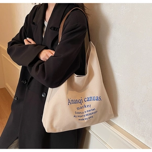 Détail d'un grand cabas en toile crème avec texte bleu et anses en cuir sur modèle