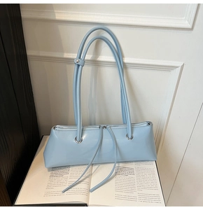 Detail of light blue leather baguette bag with silver eyelets on open book