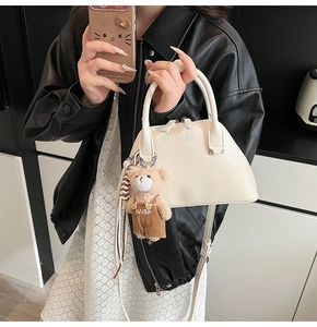Detail of white shell-shaped handbag featuring a cute teddy bear plush charm accessory