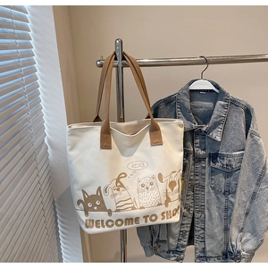 Détail du sac cabas en toile avec motif chat cartoon et anses marron sur cintre