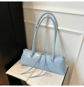 Close-up of light blue patent leather baguette bag with dual straps on an open book