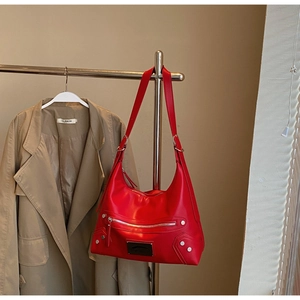 Detail view of red tote bag with silver studs and metal logo on a display stand