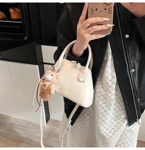Close-up of creamy white bowling bag with a cute plush bear pendant in a mirror selfie