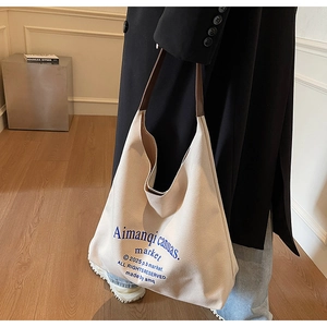 Détail du grand sac cabas en toile crème avec anses en cuir marron et texte bleu