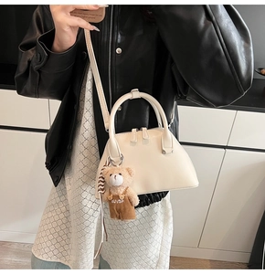 Detail of cream shell-shaped crossbody bag with a plush bear charm on a model