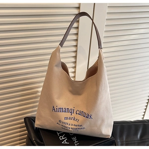 Détail du sac cabas en toile avec typographie bleue et bandoulières en cuir marron foncé