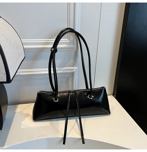 Detail view of a black glossy patent leather baguette bag with long zipper pulls