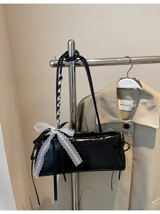 Minimalist black patent leather baguette bag with a white lace bow shown on a hanger