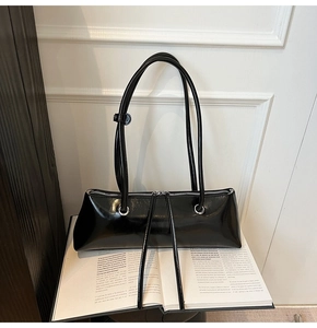 Detail of a black patent leather rectangular baguette bag on a book with silver buckles