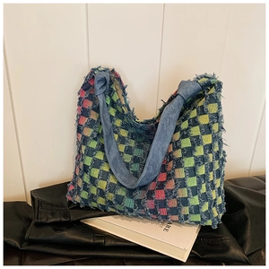 Detail of multi-color woven tote bag with fringe edges and denim handles on a leather base