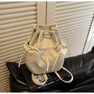 Detail of a beige PU leather bucket backpack with bow ribbons on an urban lifestyle background