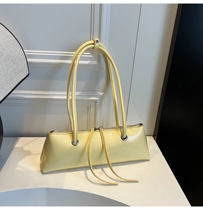 Detail of a bright yellow baguette bag showing glossy leather texture and silver eyelets