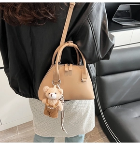 Chic beige crossbody bowling bag with a cute teddy bear charm shown on a model