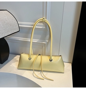 Detail of light yellow baguette bag with metal zipper and long decorative tassels