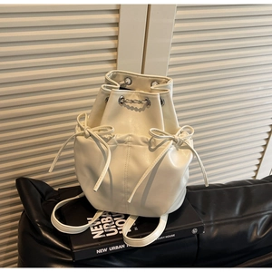 Close-up of a white leather drawstring bucket backpack featuring elegant bow details