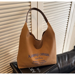 Détail d'un sac hobo en toile marron avec poignées en cuir sur un canapé en cuir noir